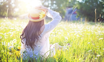 Frau mit Hut sitzt im hohen Gras an der Sonne