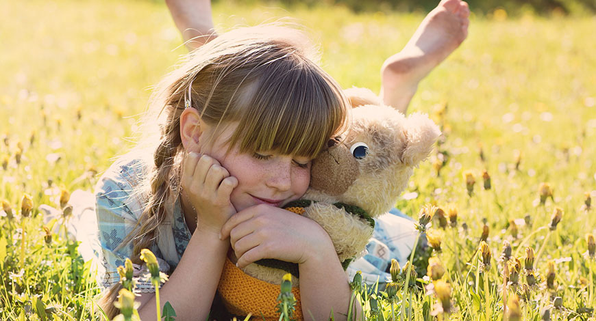 Mädchen mit Teddy im Arm liegend auf einer Wiese