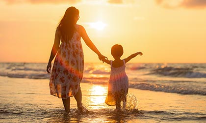 Frau mit Kind an der Hand spatziert am Strand beim Sonnenuntergang