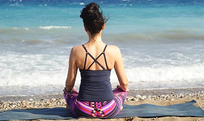 Frau sitzt au Yogamatte und schaut aufs Meer